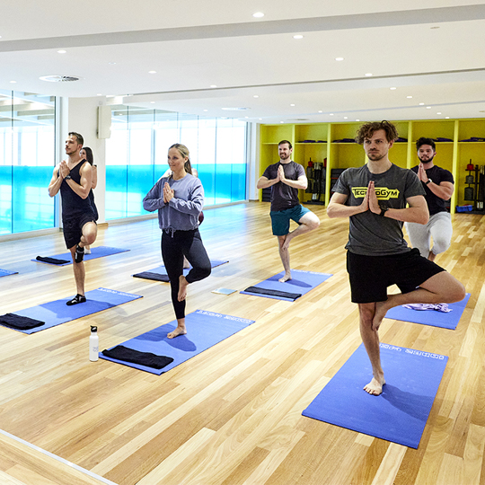 Group of people holding a yoga pose standing on yoga mats in group fitness studio
